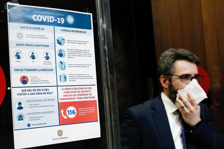 El ministre portaveu, Eric Jover, passa davant d'un dels cartells amb recomanacions sobre la Covid-19.